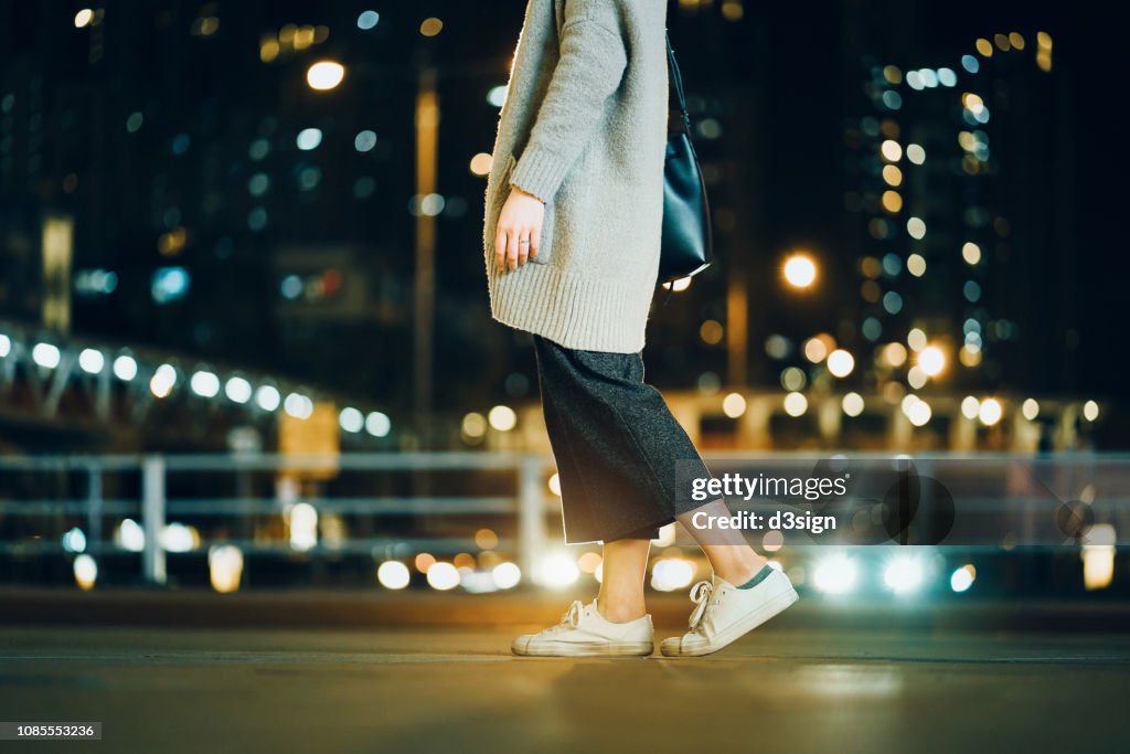 Cropped image of woman walking in the illuminated urban city at night