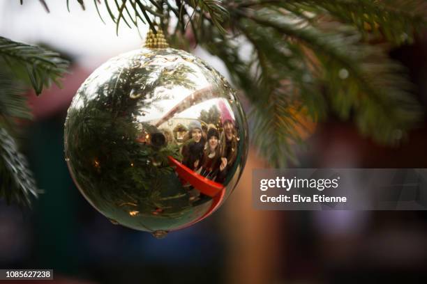 three smiling girls reflected in a shiny christmas bauble on a tree at a christmas market - naughty christmas ornaments stock pictures, royalty-free photos & images