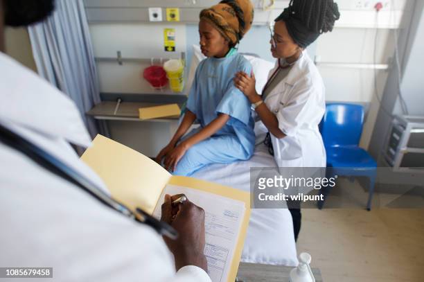 young female doctor listening with stethoscope on patient's back while notes are being taken - tuberculosis stock pictures, royalty-free photos & images