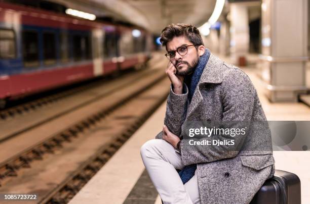 müde junger mann warten auf einen zug in der nacht. - waiting stock-fotos und bilder