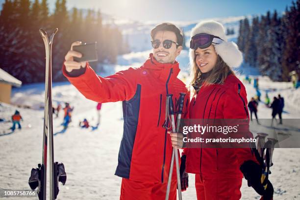 young couple is taking selfie/making video call on the ski slope - skier portrait stock pictures, royalty-free photos & images