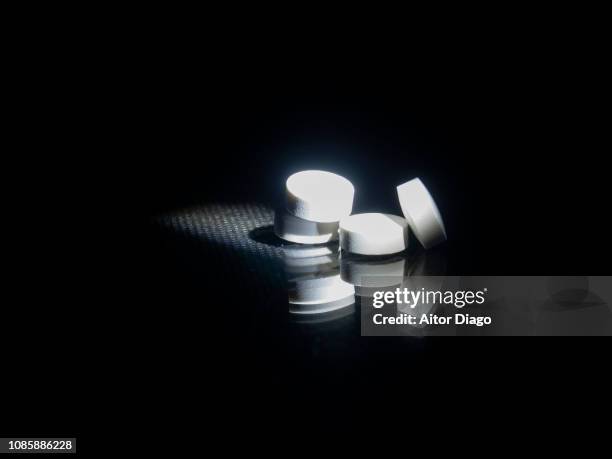 four white pills on reflective surface and black background. conceptual nature - aspirina foto e immagini stock