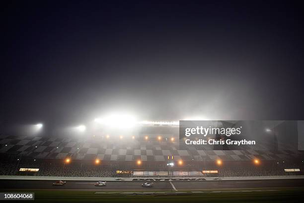 Cars race along the front stretch under caution in the early mornig fog during the Rolex 24 at Daytona International Speedway on January 30, 2011 in...