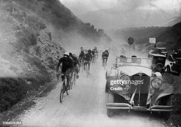 Le peloton de coureurs cyclistes monte un col, au côté d'une traction-avant, lors de la 28ème édition du Tour de France en juillet 1934. Antonin...