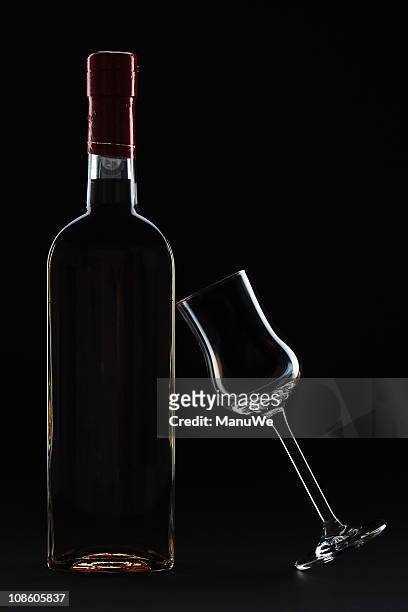 bottle grappa with leaning glass in black - grappa stock pictures, royalty-free photos & images