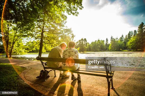 äldre par sitter på en bänk intill en sjö i en park - bench park bildbanksfoton och bilder
