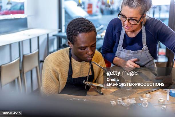 goldsmith workshop and retail shop led by independent master craftswoman with male apprentice of african origin - refugees stockfoto's en -beelden