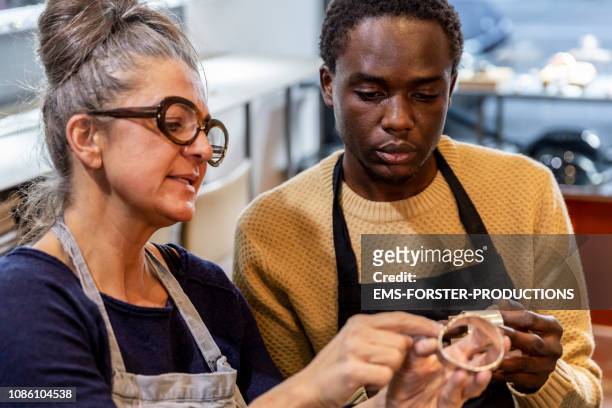 goldsmith workshop and retail shop led by independent master craftswoman with male apprentice of african origin - fugitivo stock-fotos und bilder