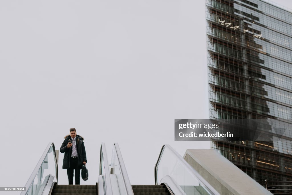 Businessman looking in his smart phone driving on an escalator