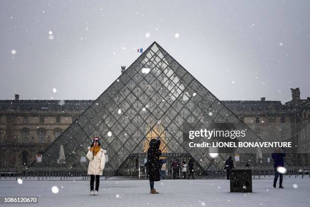 Tourists take pictures at the Louvre Pyramid as snow falls over Paris on January 22, 2019.