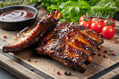 Closeup of pork ribs grilled with BBQ sauce and caramelized in honey. Tasty snack to beer on a wooden Board for filing on dark concrete background