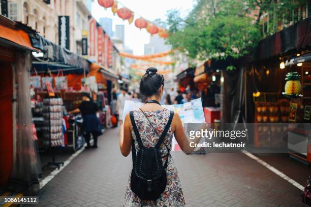 junge alleinreisende frau in singapur straßenmarkt überprüfen die map - journey stock-fotos und bilder