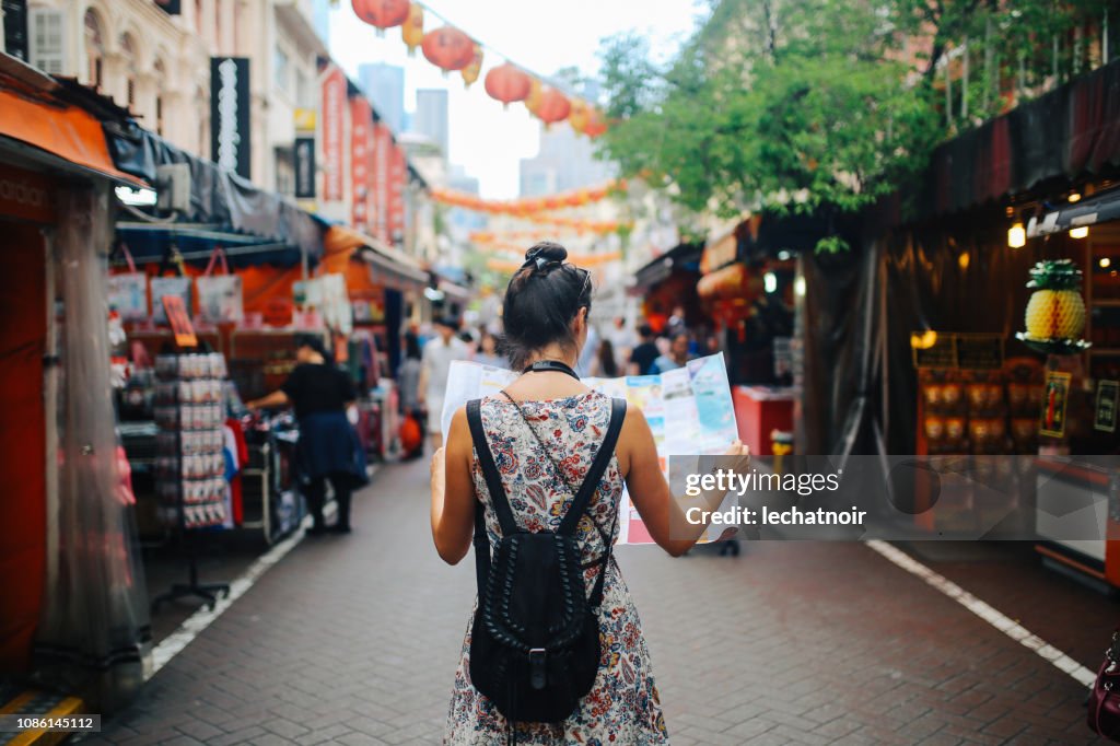 Young solo traveler woman in Singapore street market checking the map