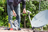 Technician installing satellite dish and television antenna on roof top