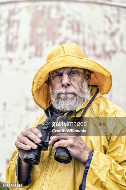 humorous sea captain holding binoculars looking at camera - rain hat stock pictures, royalty-free photos & images