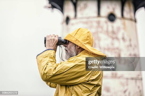 sea captain looking through binoculars near lighthouse - rain hat stock pictures, royalty-free photos & images