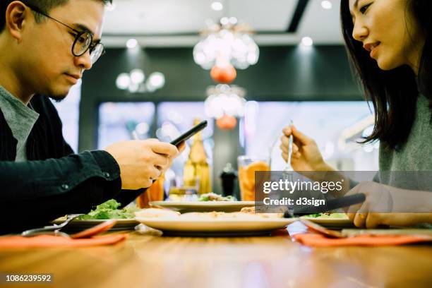 man text messaging on smartphone while having meal with girlfriend in a restaurant - dinner program stock pictures, royalty-free photos & images