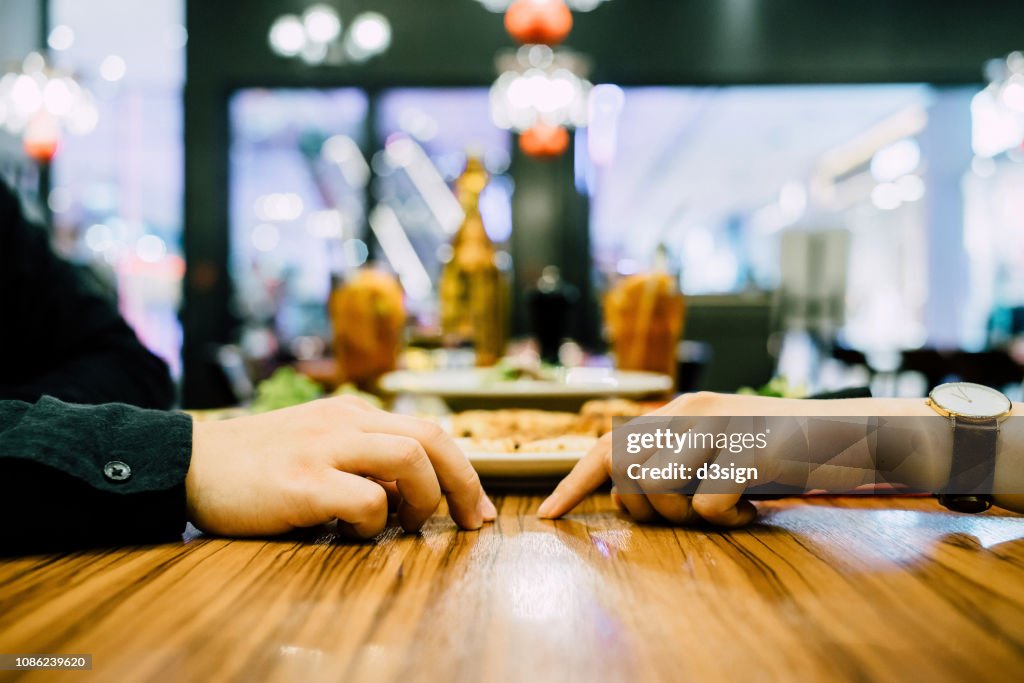 Couple going on a first date and attempting to hold hands during a dinner date at a restaurant