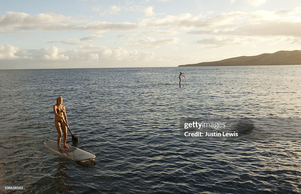 Female surger paddling a paddle board at sun set.