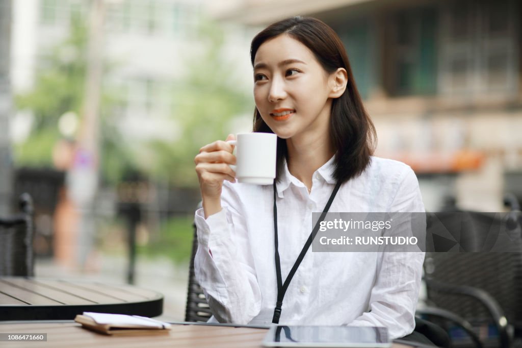 Businesswoman drinking coffee at sidewalk cafe