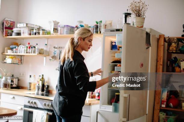 mid adult woman removing milk carton from refrigerator in kitchen at home - kitchen fridge imagens e fotografias de stock