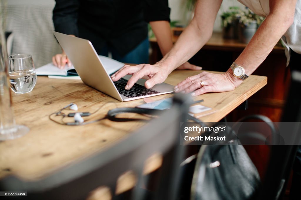 Midsection of female design professionals discussing over laptop at home office