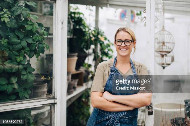 portrait of confident smiling owner standing with arms crossed at store entrance - retail occupation stockfoto's en -beelden