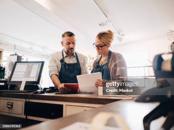 serious owners discussing over financial receipt at checkout counter in store - klein bedrijf stockfoto's en -beelden