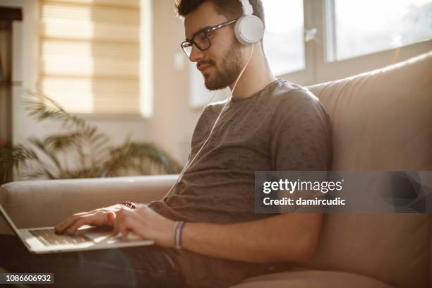 jonge man met behulp van laptop en luisteren naar muziek thuis - sync stockfoto's en -beelden