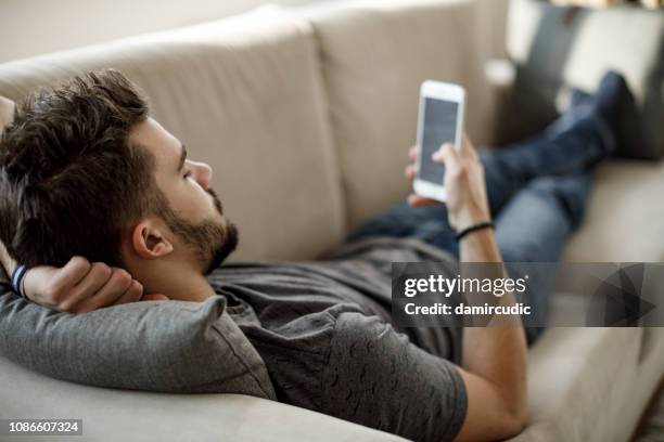 junger mann mit handy zu hause - auf rücken liegen stock-fotos und bilder