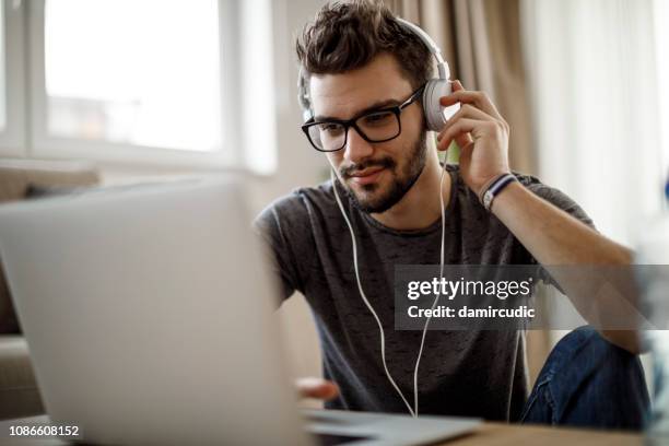 young man listening to music on laptop at home - voip stock pictures, royalty-free photos & images