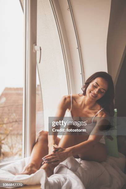 hermosa mujer masajeando las piernas por la ventana - piernas de mujer fotografías e imágenes de stock