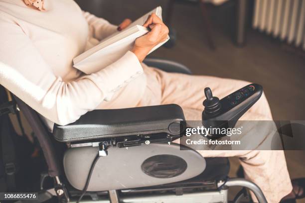 woman in wheelchair reading a book - motorized wheelchair stock pictures, royalty-free photos & images