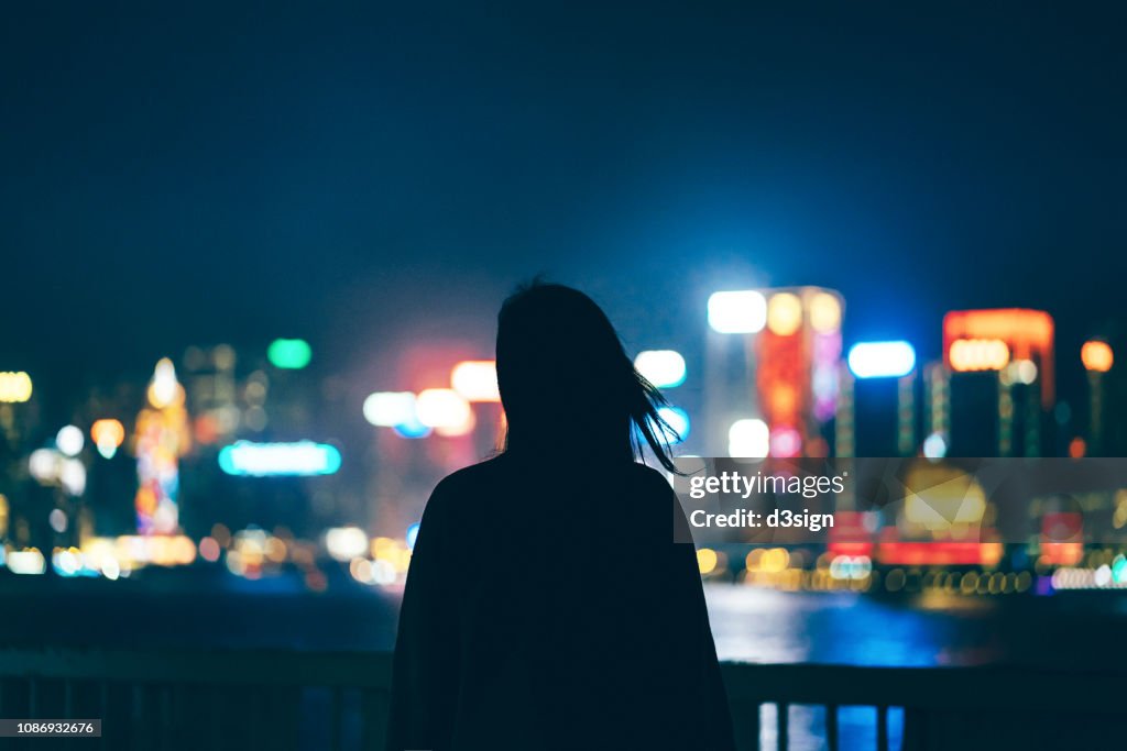 Silhouette of woman standing against illuminated and multi-coloured cityscape at night