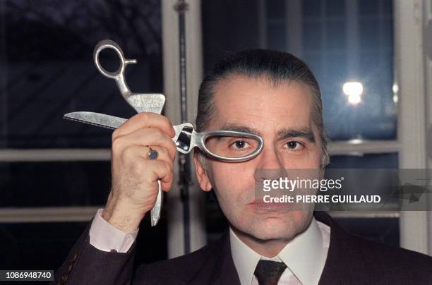 Le couturier Karl Lagerfeld pose avec une paire de ciseaux en mars 1987 dans son atelier de haute couture. German designer Karl Lagerfeld poses with...