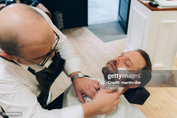 barber shaving man's beard in the barber shop - man shaving foam stock pictures, royalty-free photos & images