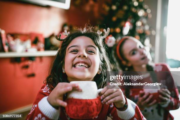 two little sisters playing around christmas tree and drinking hot beverage - eggnog stock pictures, royalty-free photos & images