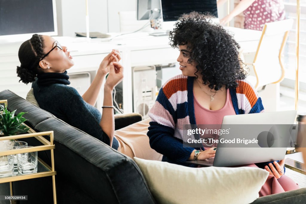Businesswomen talking while sitting on couch in office