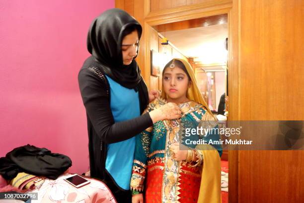 girl in hijab (veil) helping a young girl to wear traditional asian (pakistani and indian) bride dress and jewelry - punjabi girls images 個照片及圖片檔