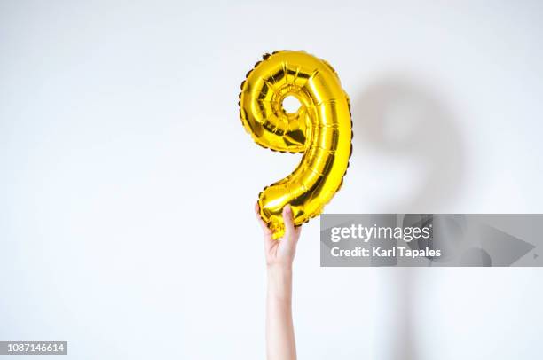 holding a golden-colored inflatable balloon number nine - number 9 stock-fotos und bilder