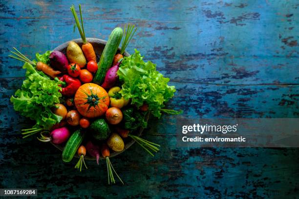 many colorful contrast color salad vegetables sitting in a round, old, wooden vegetable bowl on an abstract blue/turquoise wood rustic table background with atmospheric lighting. - tuber stock pictures, royalty-free photos & images