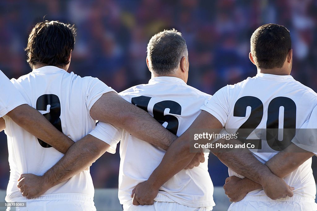 Rugby team standing with arms locked, rear view