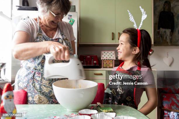 girl and grandmother look at each other whilst mixing food for christmas - summer christmas stock pictures, royalty-free photos & images