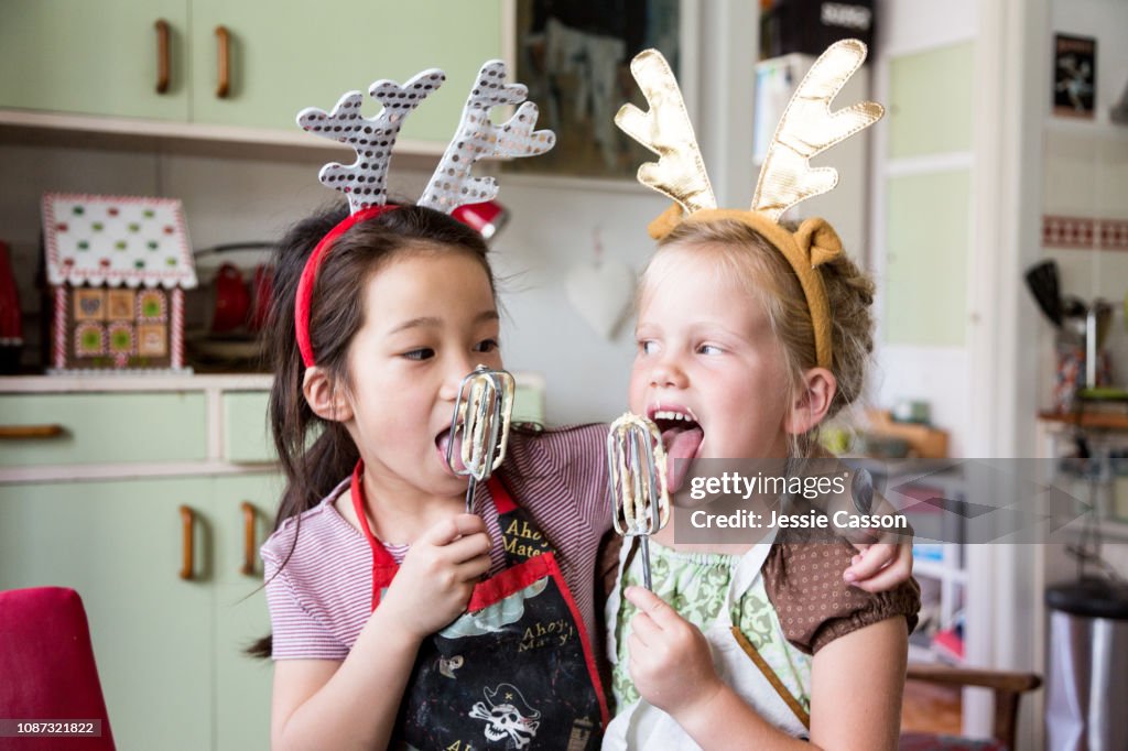 Girls tasting mix from egg beater whilst preparing food for Christmas