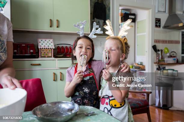 girls hugging and tasting mix from egg beater whilst preparing food for christmas - christmas family stock-fotos und bilder