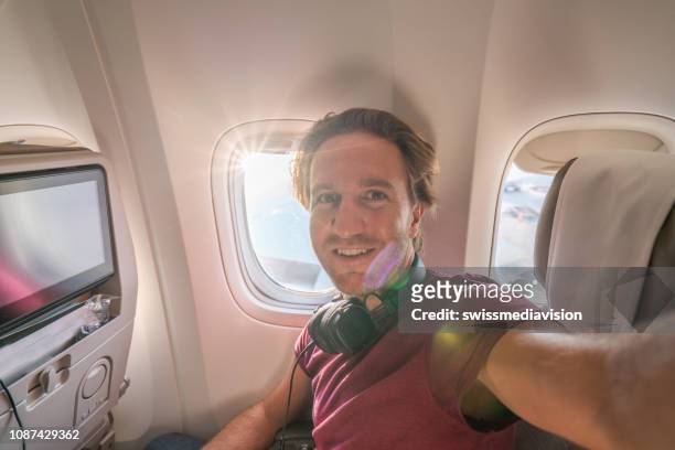 young man in airplane takes mobile phone selfie portrait during flight - selfie indoors stock pictures, royalty-free photos & images