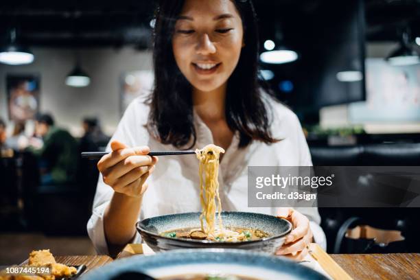 smiling young woman enjoying beef soup noodles with side dishes in restaurant - chinese soup photos et images de collection