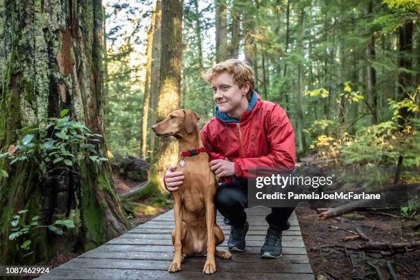 redhead teenaged boy with vizsla dog resting on forest boardwalk - vancouver canada 2018 stock pictures, royalty-free photos & images