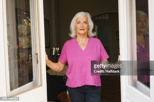 portrait confident senior woman standing in patio doorway - man opening door woman stock-fotos und bilder