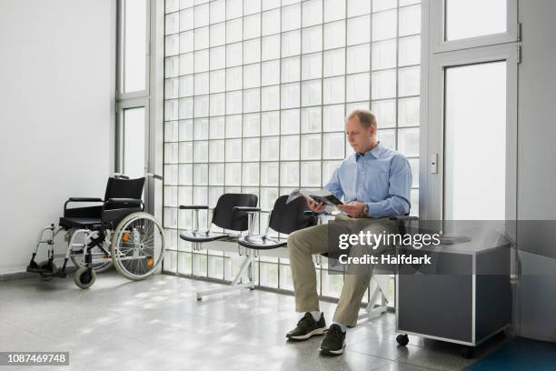 male patient waiting, reading magazine in clinic waiting room - hospital waiting room stockfoto's en -beelden